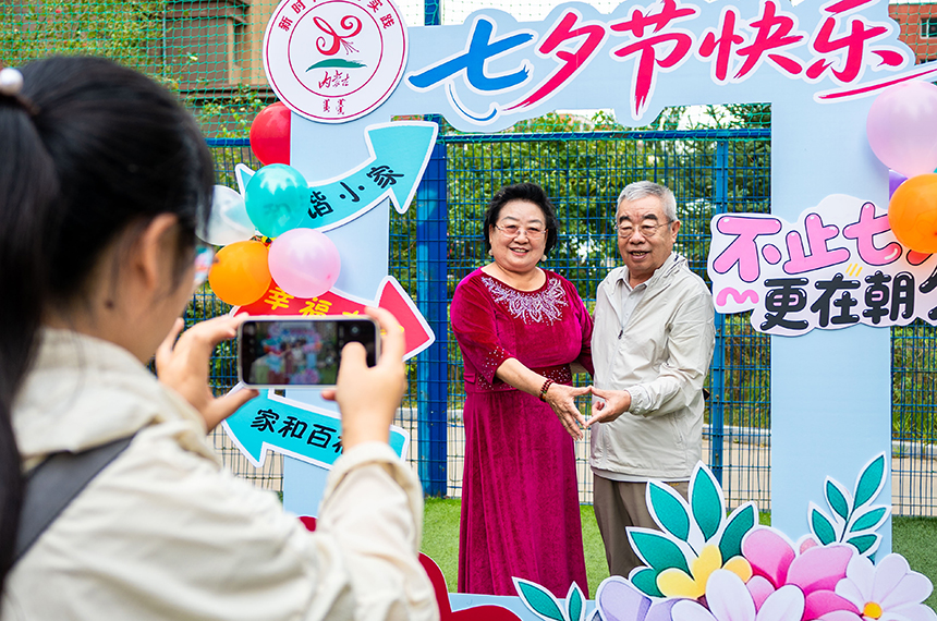 呼和浩特市玉泉区“爱在‘七夕’践文明 和谐家风共传承”主题文明市集活动现场，志愿者在为老年夫妻拍摄“七夕”纪念合影。丁根厚摄